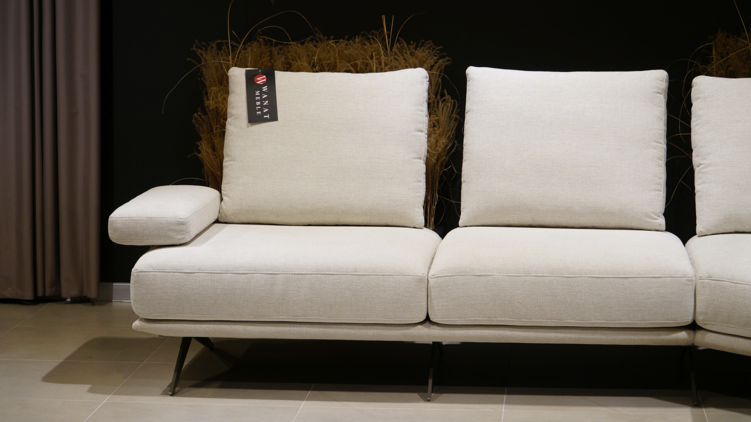 Designerski narożnik do salonu w jasnobeżowej tapicerce materiałowej z otwartym szezlongiem i minimalistyczną podstawą na cienkich nogach